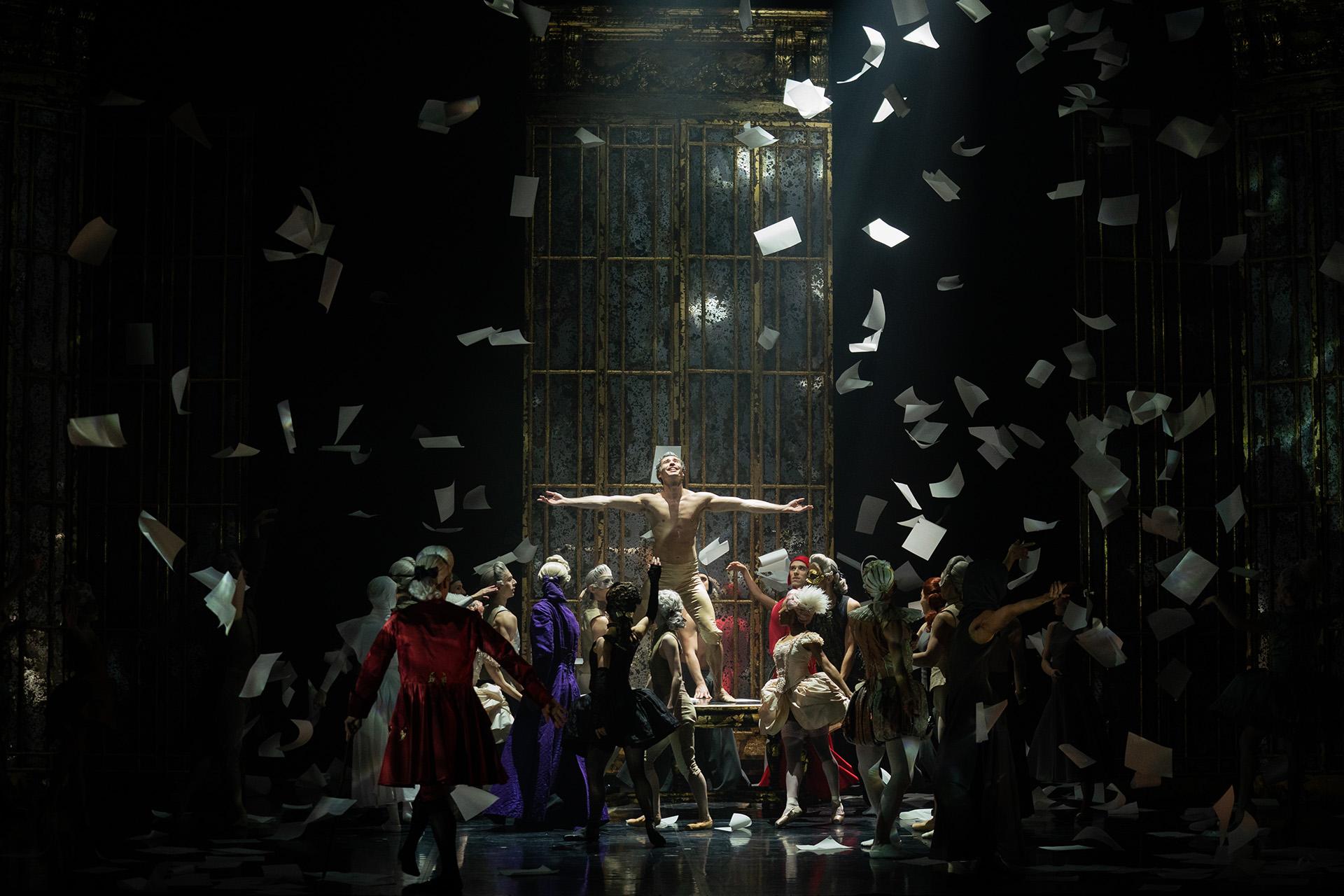 Man standing on a table, surrounded by a host of people, sheets of paper, his memoirs, raining down on them