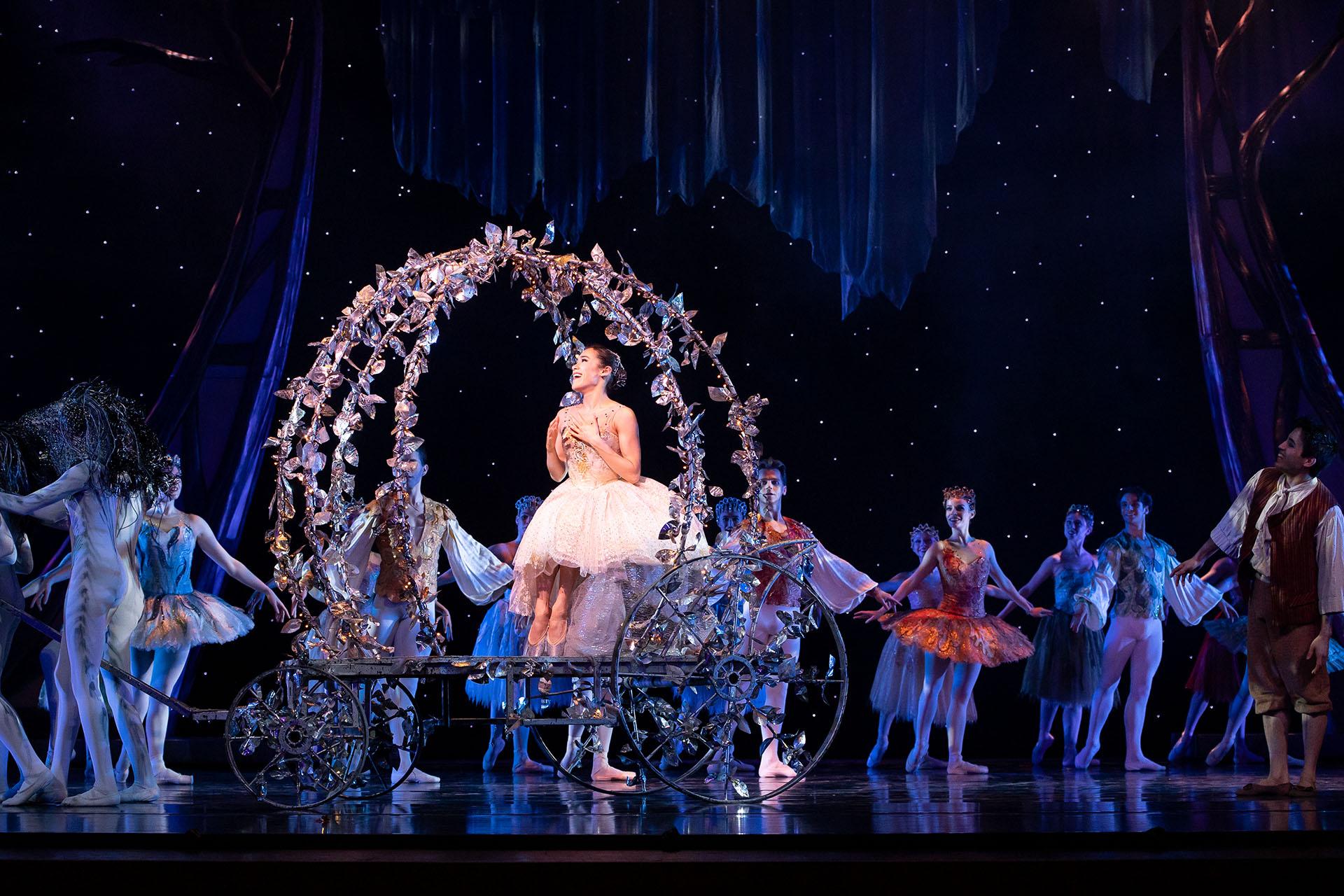 Dressing white, a dancer rides an open, decorated carriage surrounded by onlookers