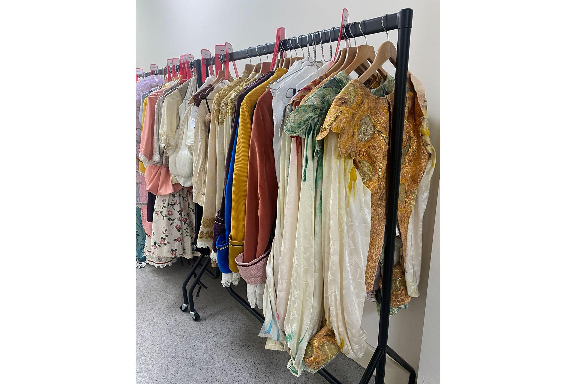 A wardrobe rail filled with male and female costumes for Cinderella, full of cream, gold, green and pink