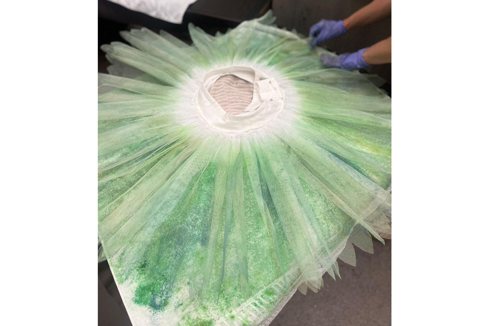 A green tutu being dyed by gloved hands in Wardrobe