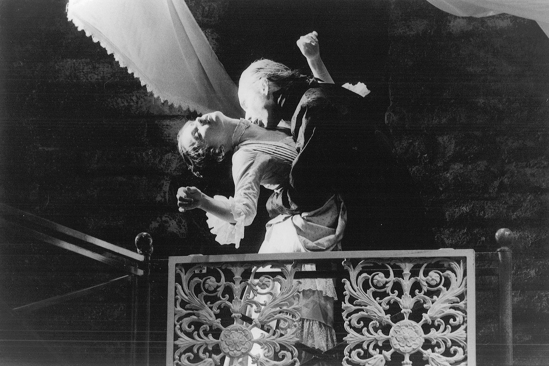In black and white, a woman stands in Dracula's arms with her head tilted back as he bites her neck