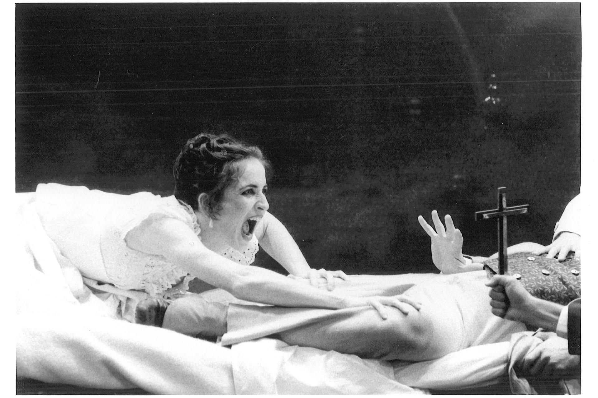 In black and white, a woman screams in despair as a cross is held up.