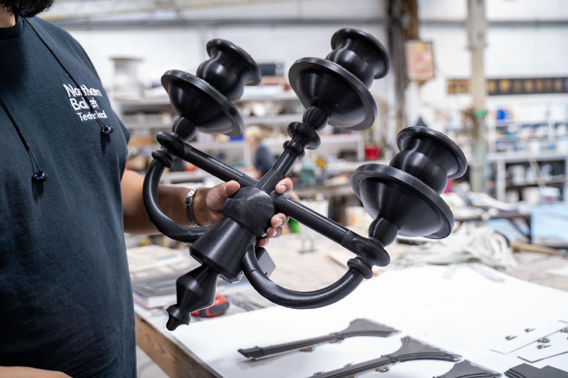 A man in a black shirt holds a large 3D-printed candelabra.