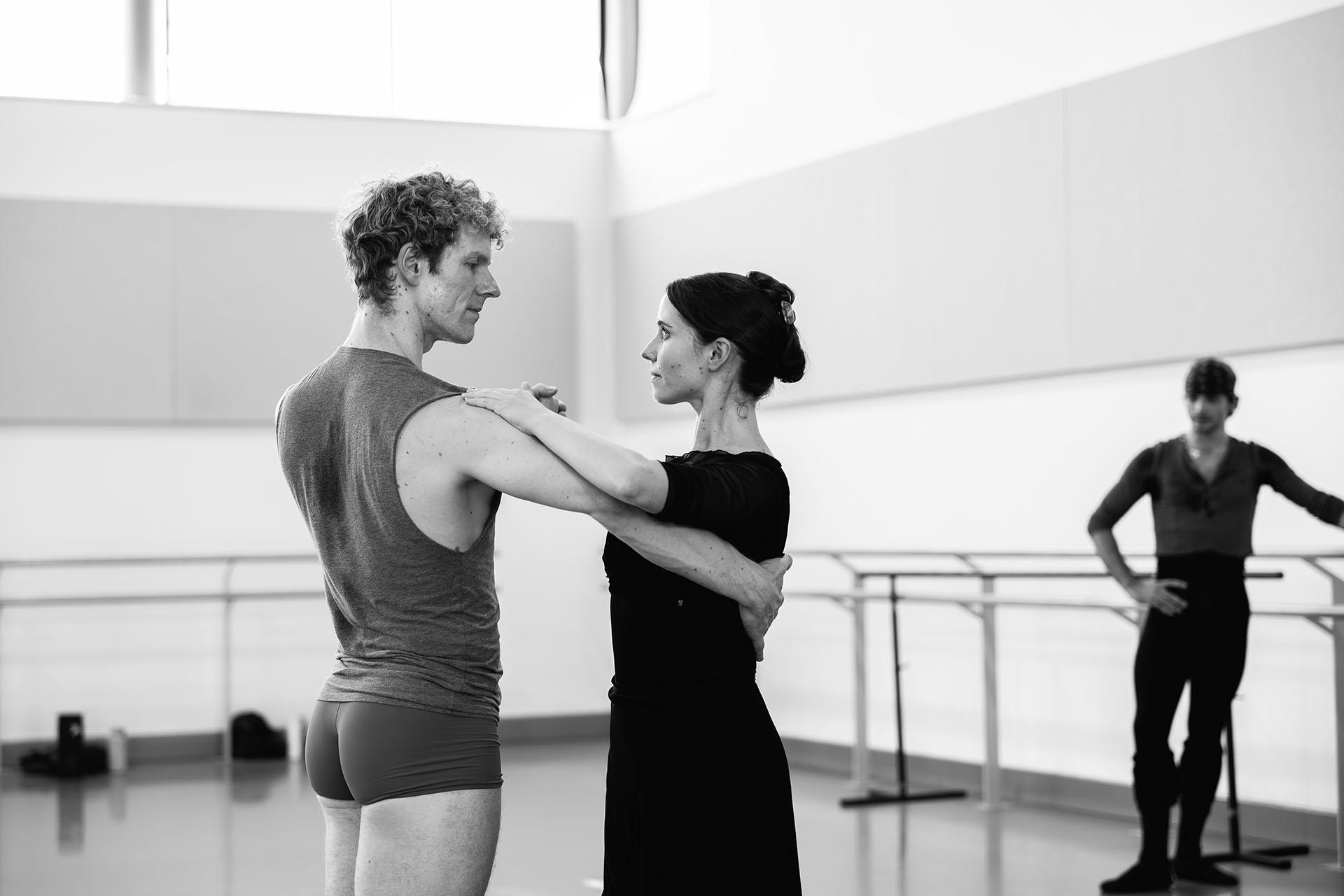Two dancer in the rehearsal room practicing a tango, bodies apart, one hand holding the partner's, her other hand resting on his shoulder, his on her back, each looking intently at the other