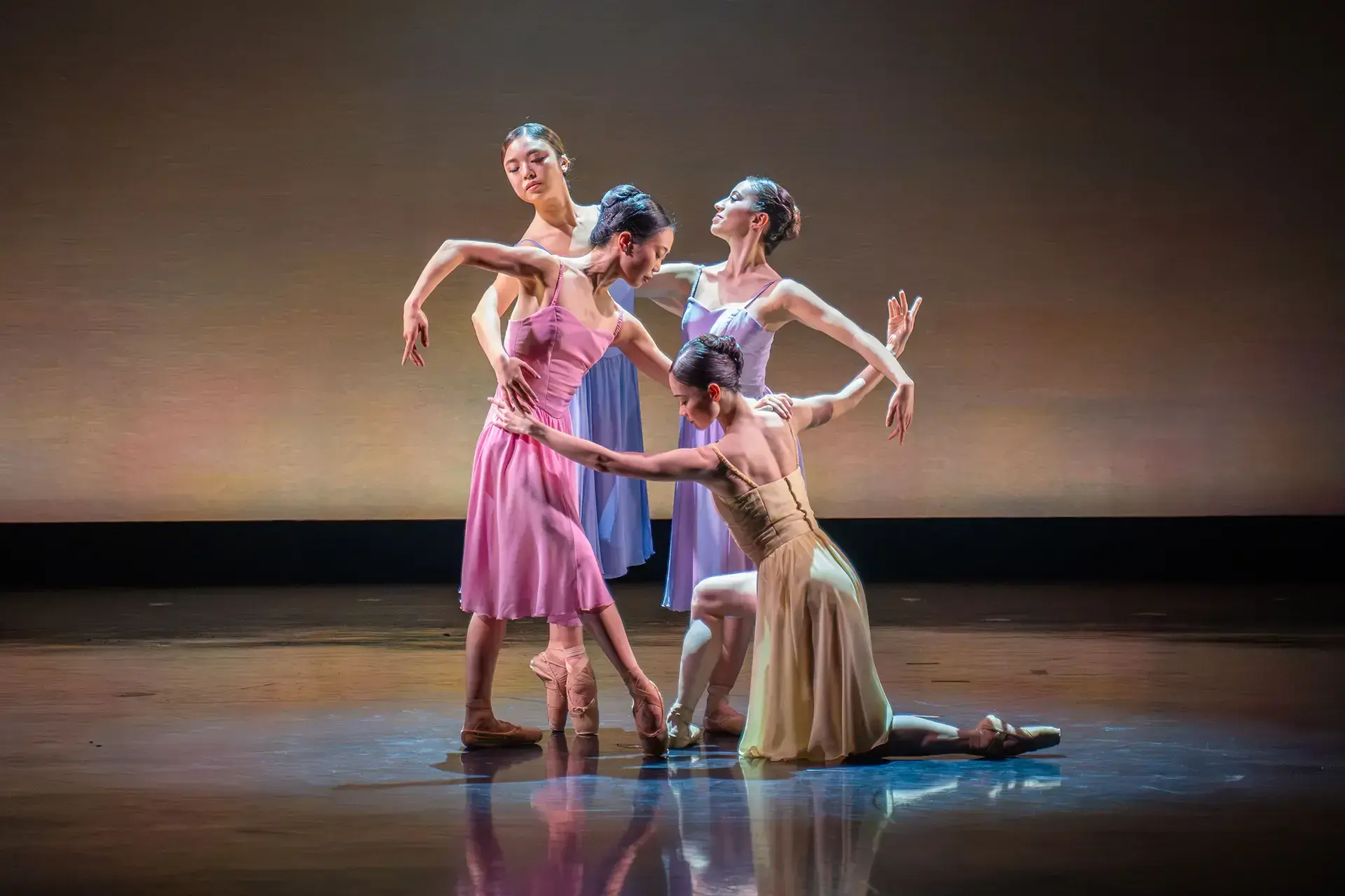 Four dancers standing close, one on a knee, another holding her shoulder