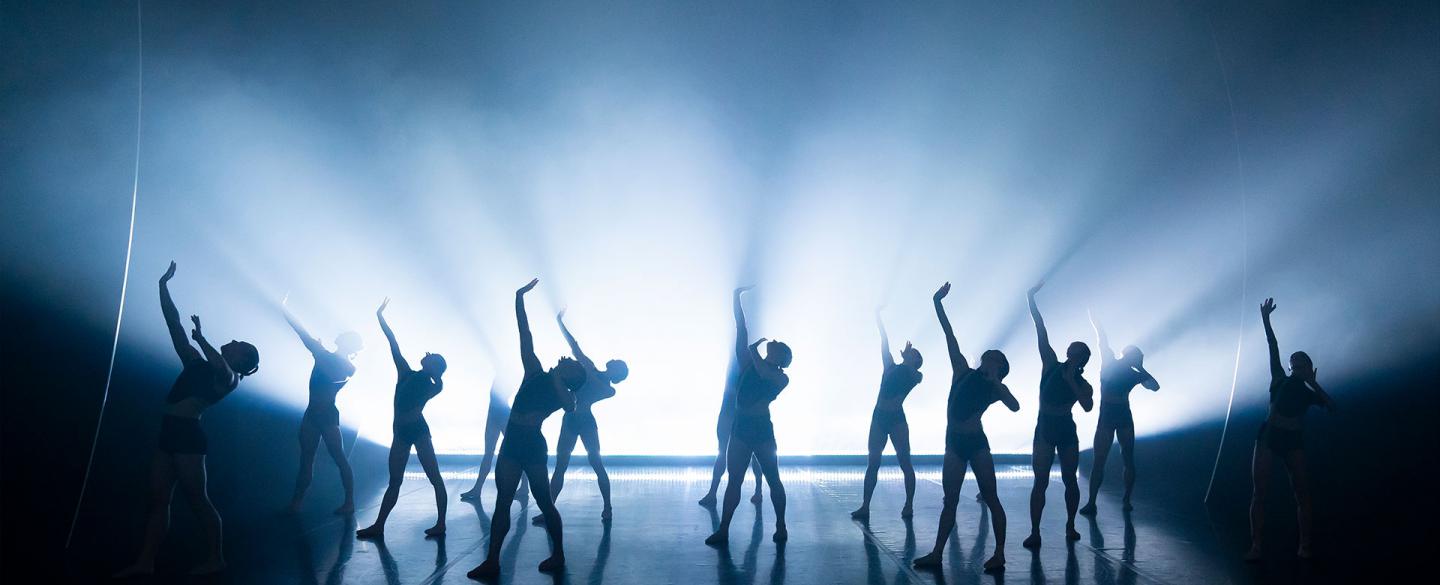 A group of dancers with intense lighting behind