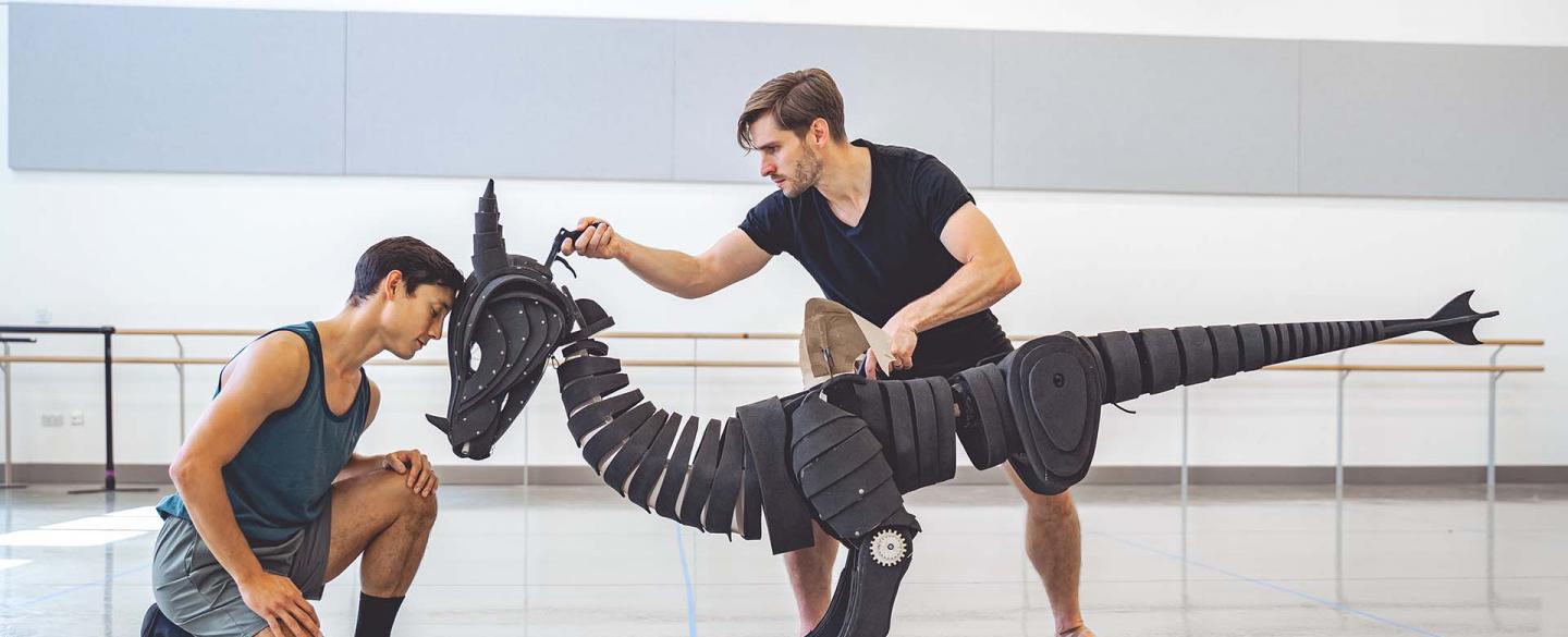 A dancer rests his forehead against a dragon puppet's forehead, the dragon puppet controlled by a second dancer