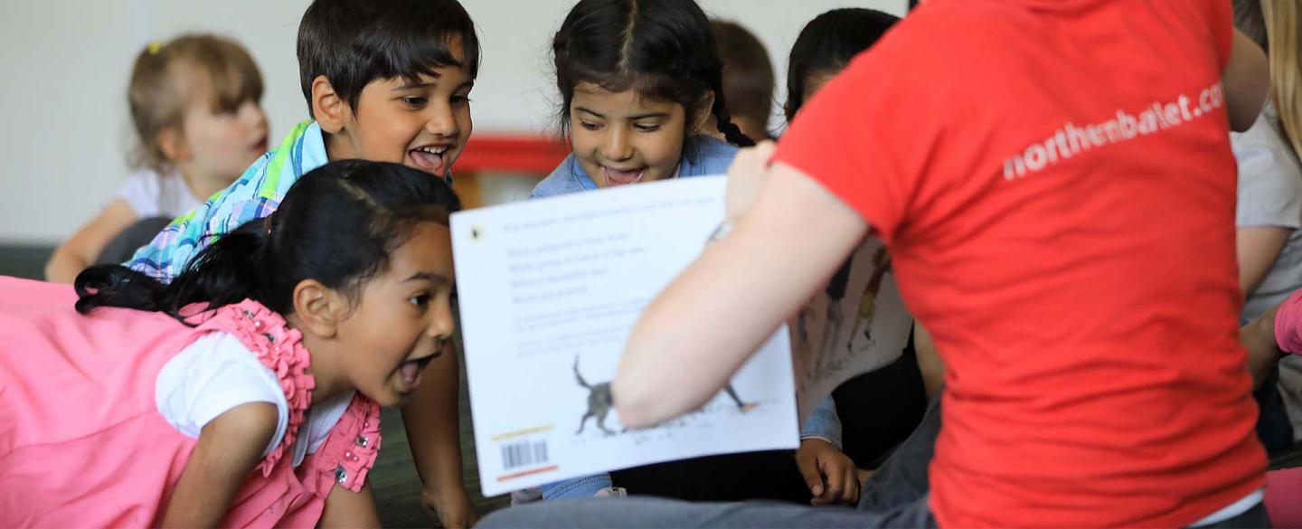 Children are excited at the contents of a book being shown to them by a Dance Education Officer