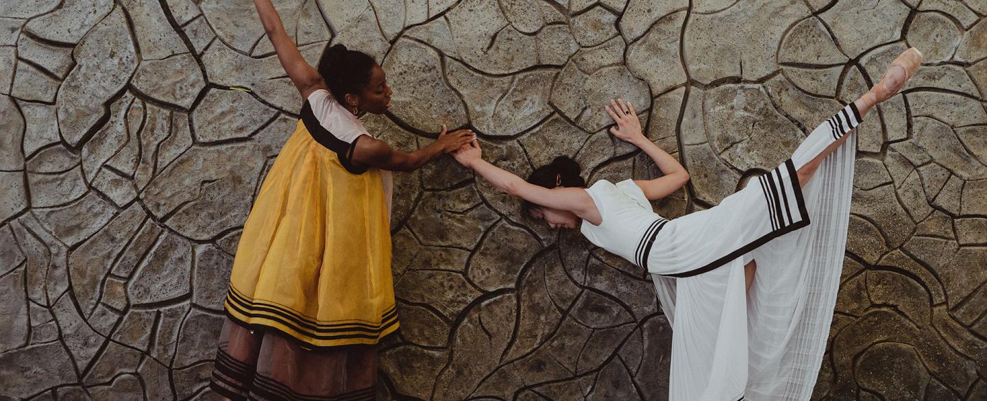 Two female dancers reach out to a cracked wall