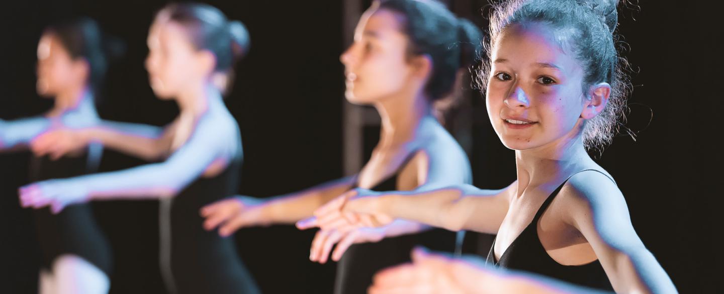 A little girl in a ballet show turning towards the camera smiling