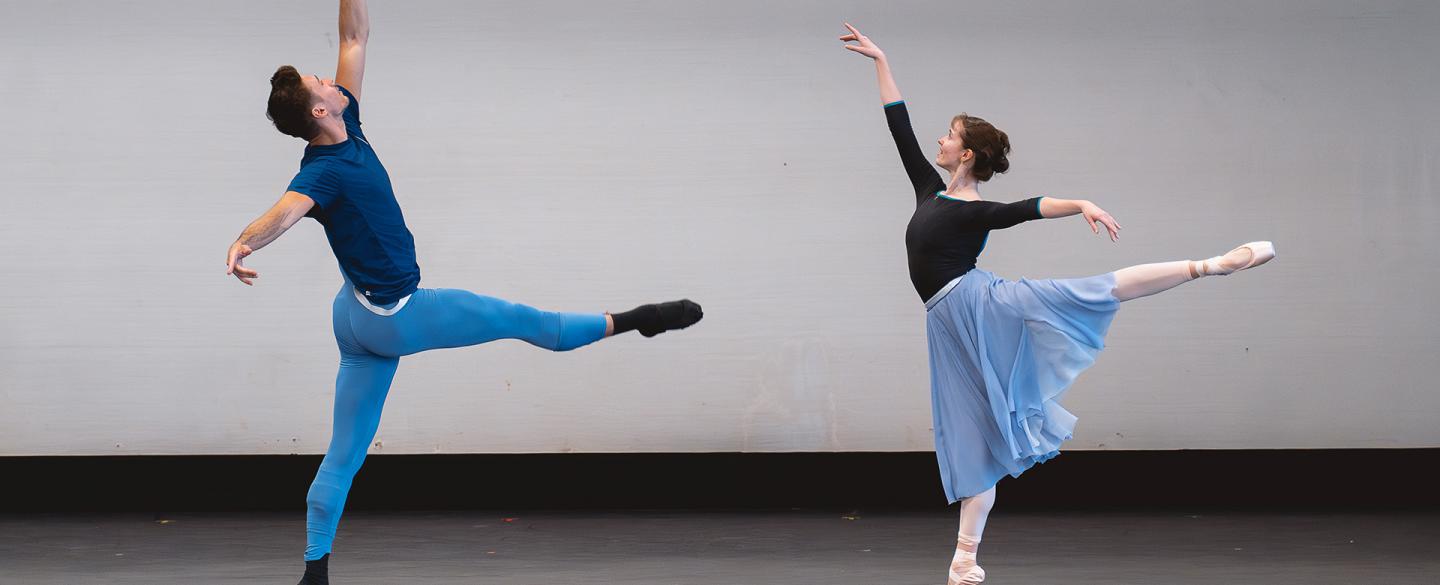 Two dancer striking similar poses, both on one leg, the male to the left has a leg perpendicular to his body in from of him, and the female to the right is perfectly arabesque