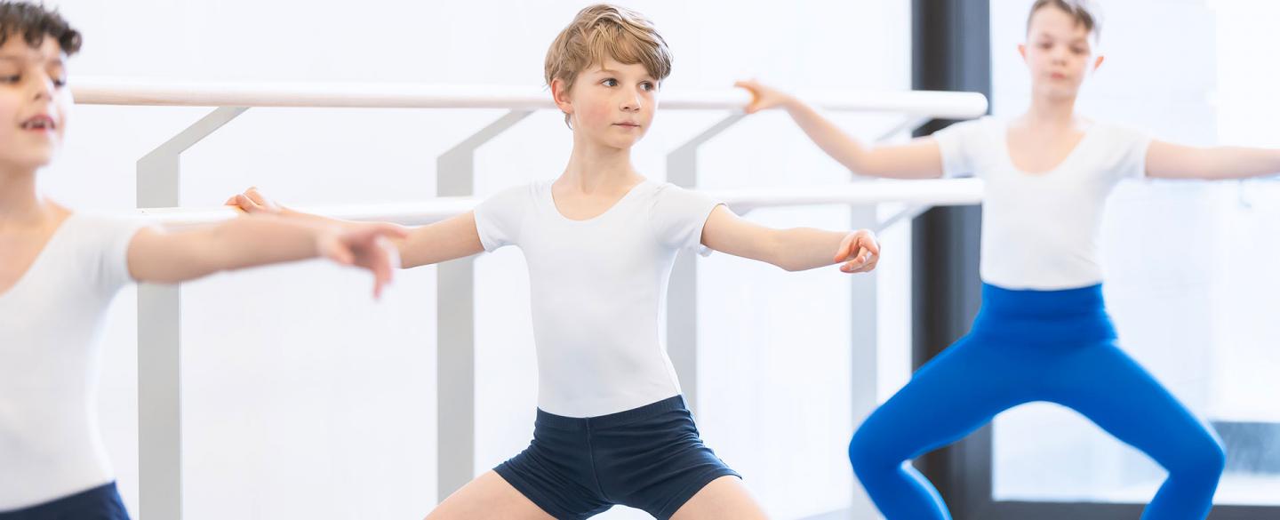 Boy at the barre, holding himself steady and his knees bent out.