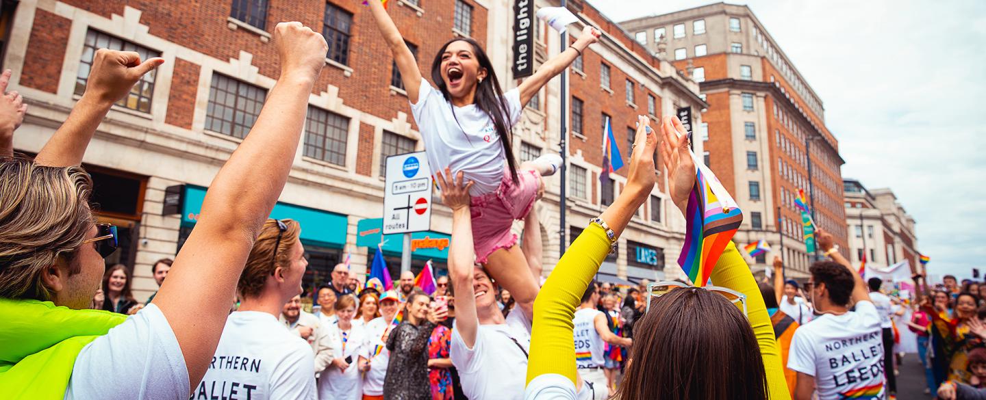 Laughing woman with long dark hair lifted by overhead with her arms raised in celebration