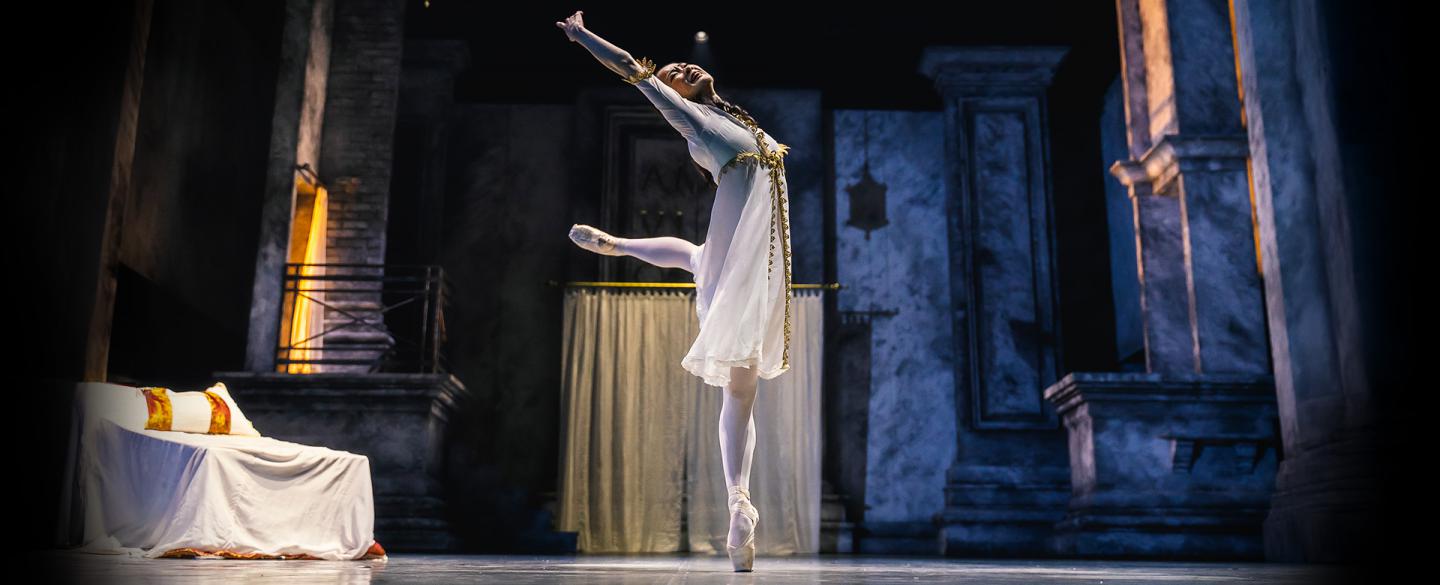 Juliet in white standing en pointe, happily reaching upwards