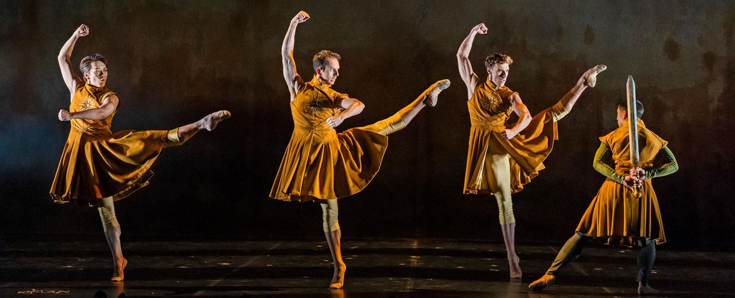 Three men in golden uniforms standing on one foot, their other leg raised, straight at the knee and one arm aggressively above their head, a fourth man is stood facing in a different direction wearing the same uniform but holding a sword behind his back