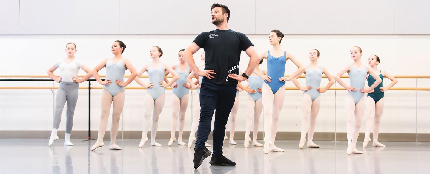 Teacher stands in front of a class, hands on hips, one foot extended and the many students behind him copying