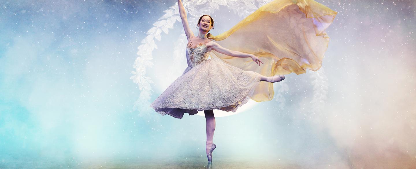 Against a blue and golden fantasy background, a woman stands on one pointed foot, one hand in the air, her other leg balanced elegantly behind her as her dress flows behind her