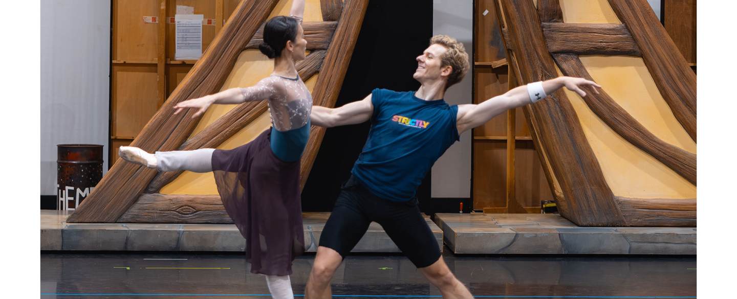 A dancer en pointe arabesque, the other steadying her balance with one hand holding her back and leaning back theatrically