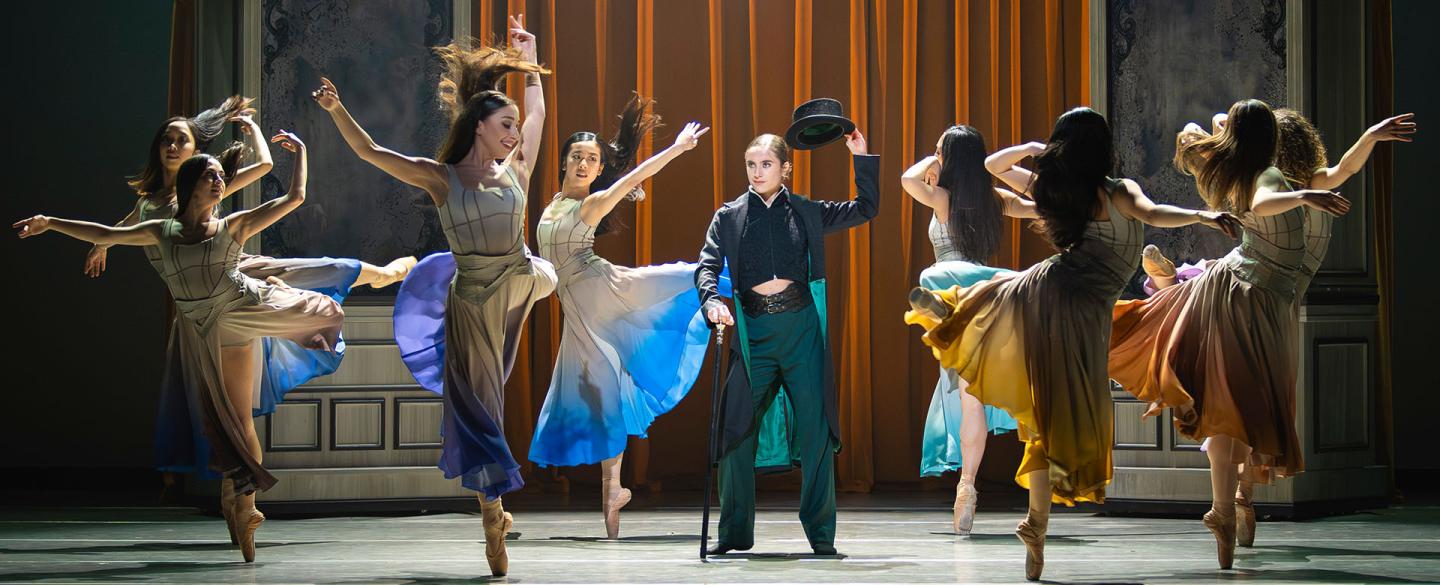 In a dressing room a group of women wearing similar dresses with different accent colours dance around Anne Lister who lifts her hat in respect to them