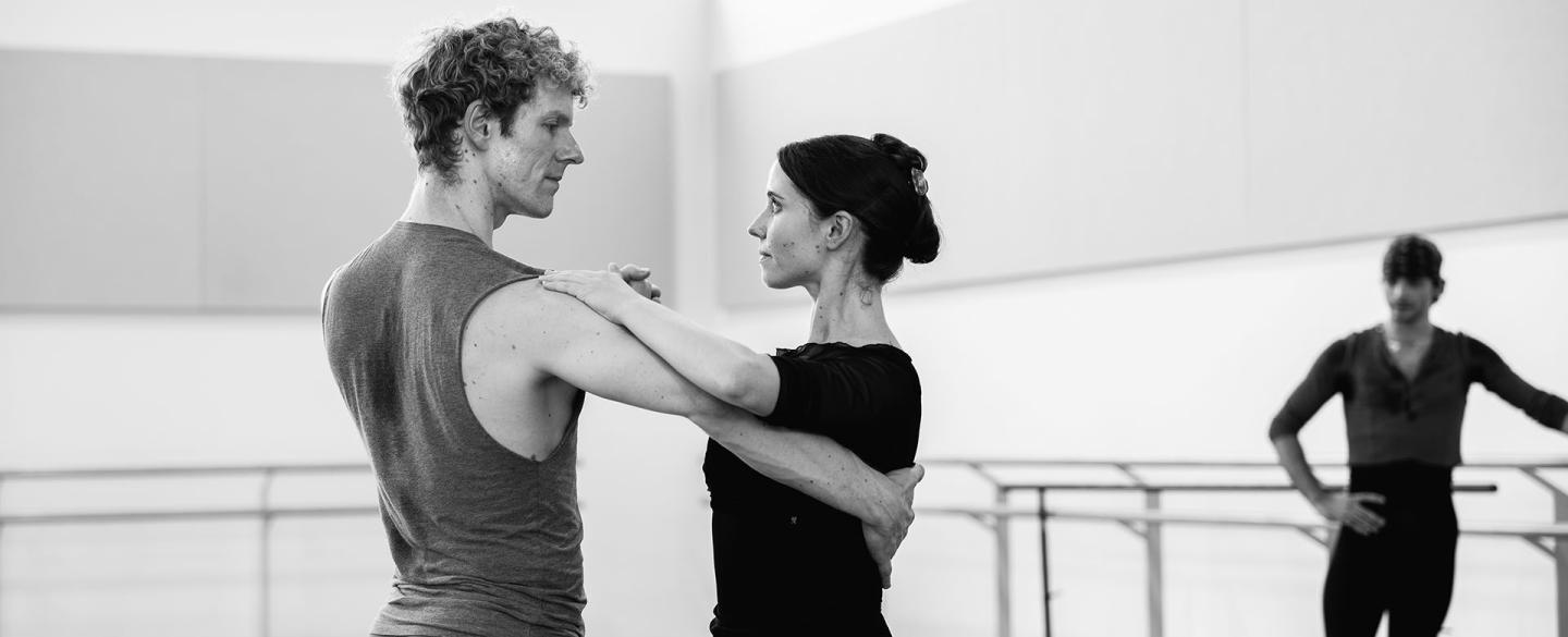 Two dancer in the rehearsal room practicing a tango, bodies apart, one hand holding the partner's, her other hand resting on his shoulder, his on her back, each looking intently at the other