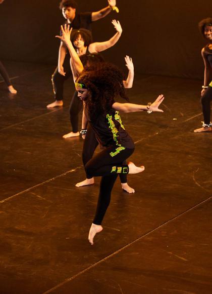 A group of dancers dressed in black with green and black patterned highlights performing on a dance stage