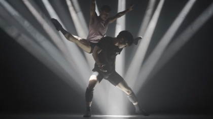 Beams of light focus on one spot. One dancer stands above it. A Second dancer leaps behind him, legs and arms spread apart.
