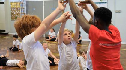 Male children reach up with a Dance Education Officer in a dance being taught to them