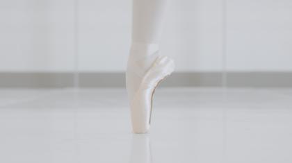 A single foot stands en pointe on a white studio floor.