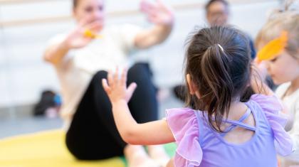 A little girl in a purple leotard reaching to her dance teacher in class