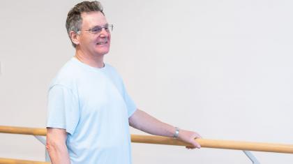A man stood smiling, holding onto the ballet barre
