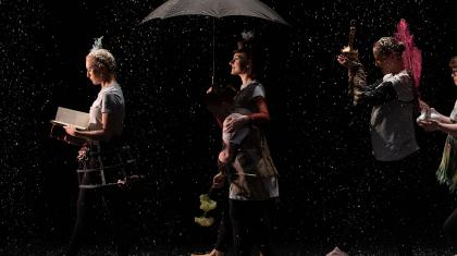 One person walk while reading a book, following her a dancer carrying a doll and an opened umbrella