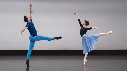 Two dancer striking similar poses, both on one leg, the male to the left has a leg perpendicular to his body in from of him, and the female to the right is perfectly arabesque
