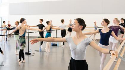 Students in a dance studio stand at bars and practice their poses