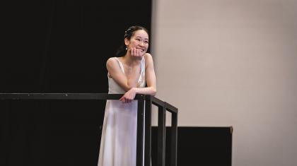 A dancer on a balcony dresses all in white smiles while resting a hand on her chin