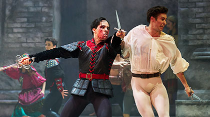 Dagger in one hand, sword in the other, Tybalt has blood on his face but swings wildly for his opponent