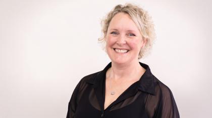 Blonde woman smiling broadly, wearing a black shear shirt unfastened at the collar