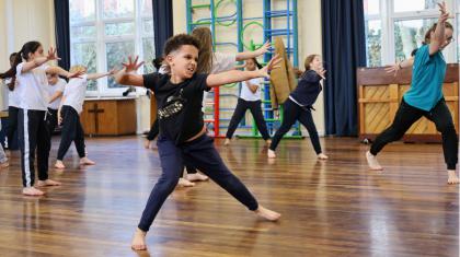 A class of young students stand with legs apart and push forward with open palms.