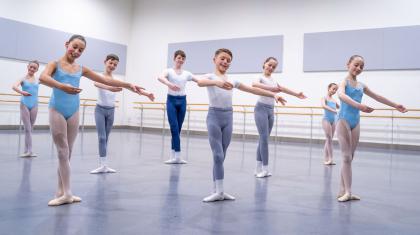 Eight children, mixed genders, holding a similar pose and smiling as they take part in a class