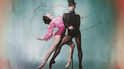 Wearing a black top hat and pointe shoes, the character of Gentleman Jack looks directly at the camera hands on a cane, a woman in pink hold onto her and leans back suggestively