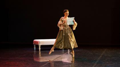 Dancer in French Regency attire and on pointed feet reads a letter