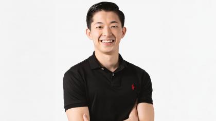 Man in black top with dark hair looking and smiling directly at the camera