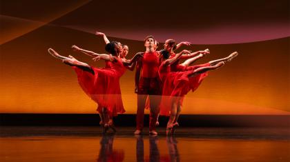 Dancers in red, either side of the central figure people stand arabesque