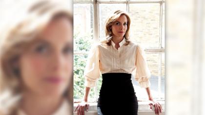 Dame Darcey Bussell in a high-waisted black skirt and white shirt leaning against a window bright with summer sun