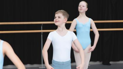 Male student in grey leggings and white t-shirt standing in first position in the training studio