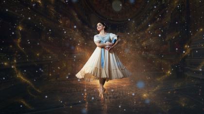 A dancer in Edwardian costume hold a Nutcracker doll in her arms, stands en pointe and smiles with childlike wonder