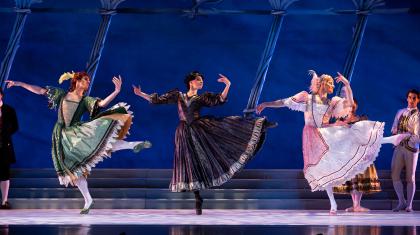 Three women, one in green, one in black, the other in pink, dance in unison