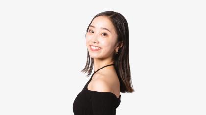 A dancer stood side on, looking at the camera wearing a black top and dark hair.