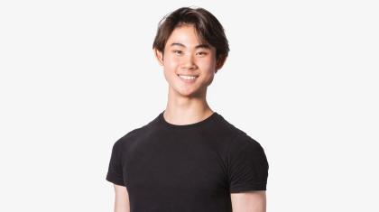 A man with short brown hair stood on a white background wearing a black t-shirt.