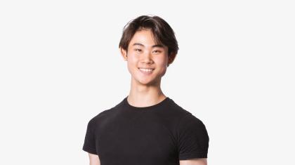 A man with short brown hair stood on a white background wearing a black t-shirt.