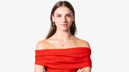 Woman with long, straight, dark hair, wearing a vivid red top, looks directly at the camera